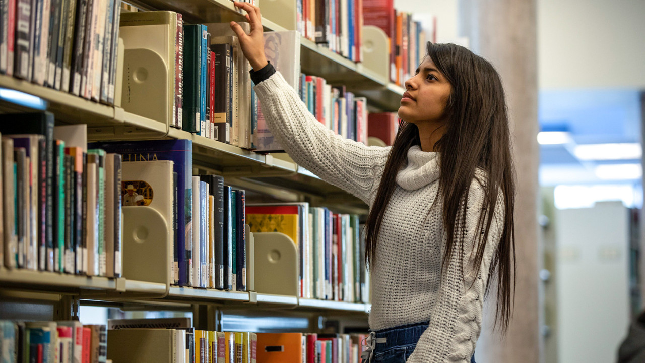 A young woman searches for a book the Library stacks