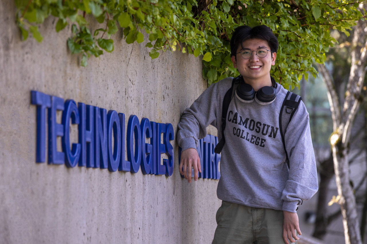 A technology student stands out front of tech building sign on interurban campus